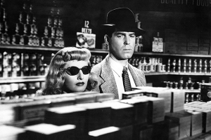 a short blond woman in sunglasses looks over an aisle while a taller man wearing a hat looks at boxes